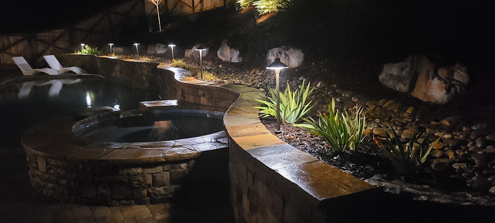 Backyard pool and spa illuminated with warm landscape and path lighting at night by Lightech
