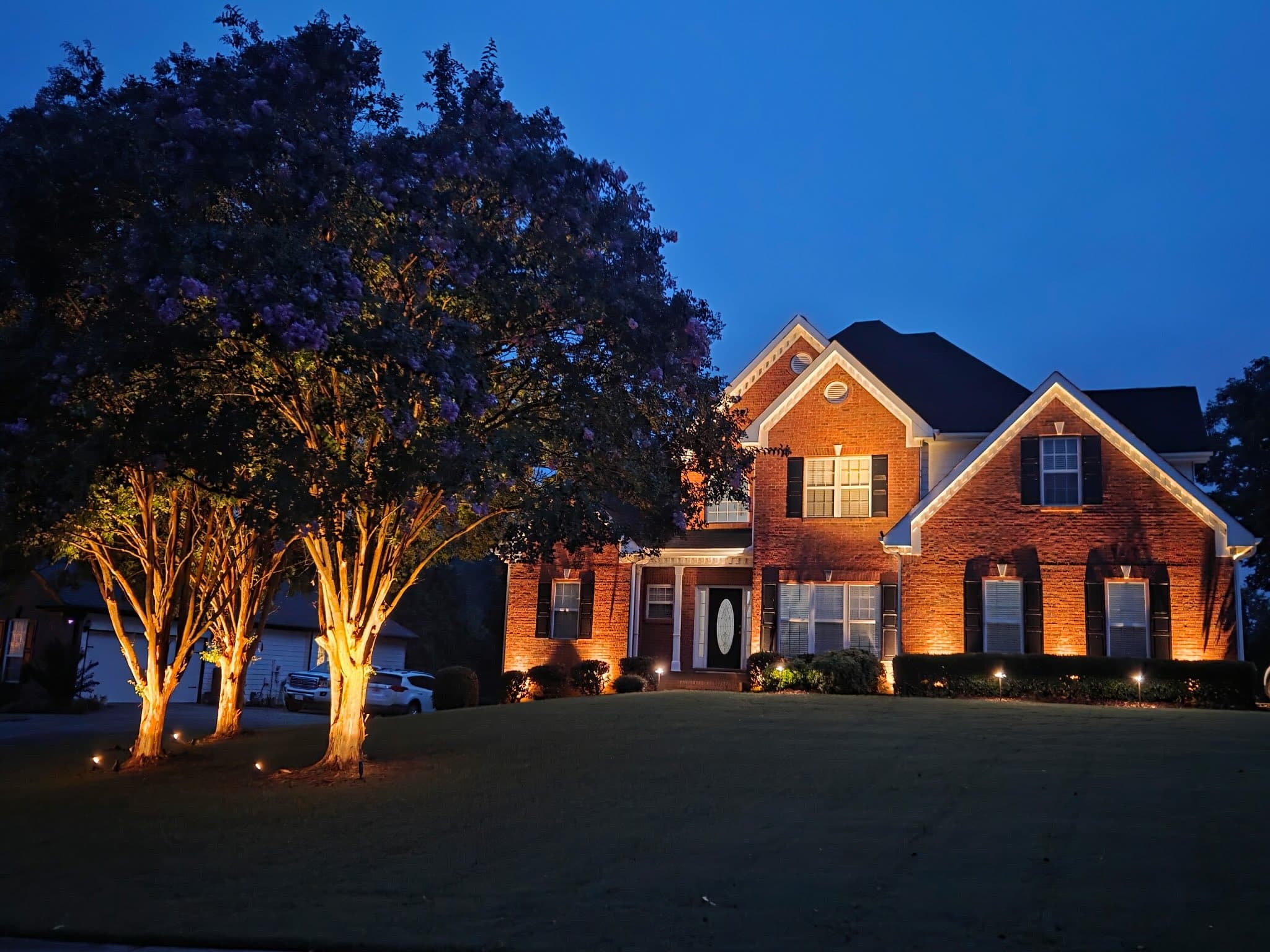 Two-story brick North Georgia home in Hoschton with layered landscape and facade lighting at dusk