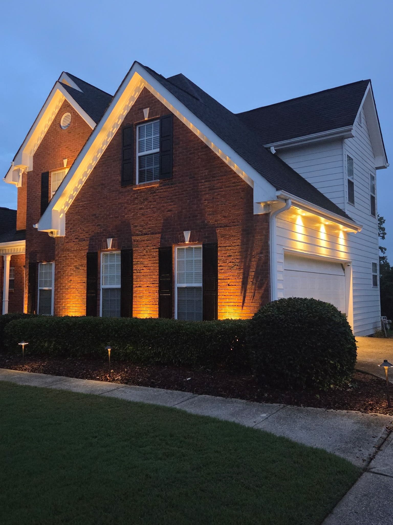 Two-story brick North Georgia home with warm roofline and soffit lighting outlining every gable at dusk