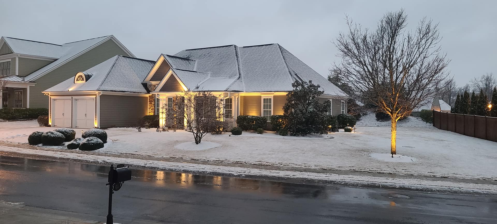 Ranch home in light snow with warm lighting along the roofline at dusk